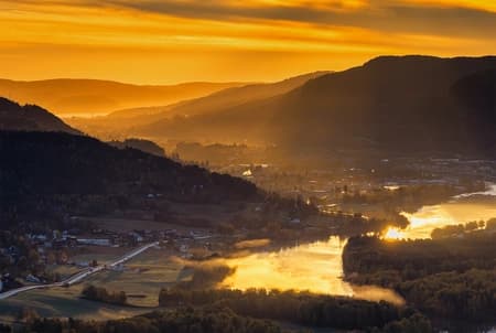 A long-lens aerial capture from above Hokksund, looking east through the Drammenselva valley toward Mjøndalen and the port of Drammen.